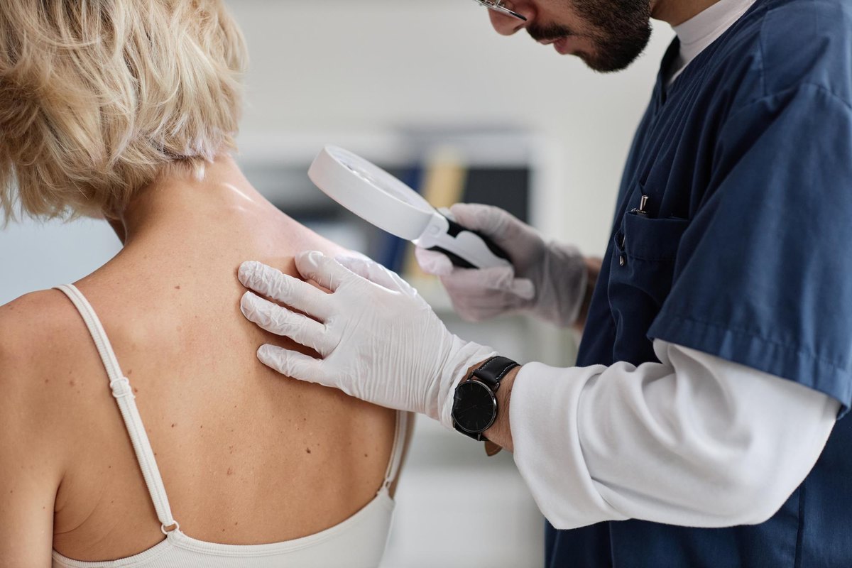 Dermatologist using a magnifier to examine light patches of skin discoloration on a patient's shoulder and back